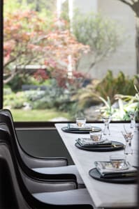 Modern dining room featuring a marble table set for a meal with greenery in the background.