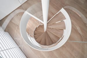 A modern, circular staircase featuring wooden steps and glass railings within a contemporary architectural setting.