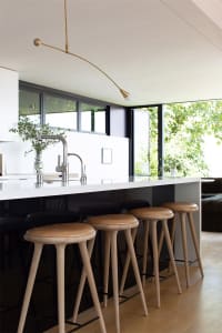 A modern kitchen featuring wooden stools and a white countertop with a sink and faucet.