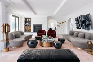 Modern living room featuring grey sofas, red accent chairs, and black side tables, with a fireplace and large windows.