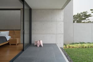 A modern minimalist residential interior featuring a concrete wall and floor, with a pink elephant stool outside.
