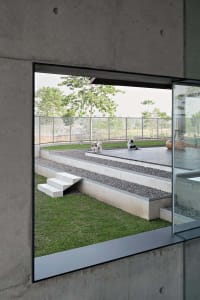 Modern landscape with concrete steps, gravel pathways, and green grass surrounded by a metal fence and trees in the distance.