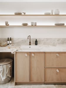 A modern minimalist kitchen with wooden cabinets, marble countertops, and a sink with a bronze faucet.