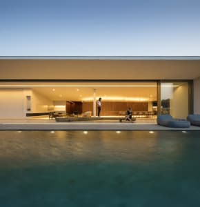 A modern residential poolside area with concrete walls and large glass doors.