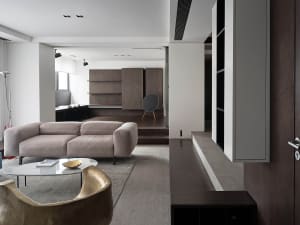 A modern living room with a beige sofa, a round coffee table, and a round speaker on a wooden shelf.