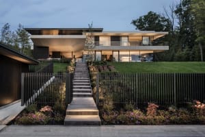 A modern, two-story house with large windows and a wooden staircase leading up to it.