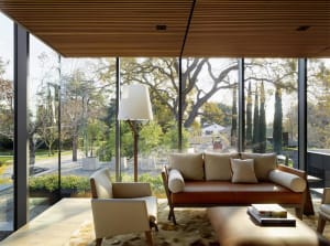 A modern living room featuring wooden walls and a brown leather sofa, with a large window showcasing a serene outdoor landsca