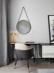 A modern minimalist home office desk with a round mirror, leather chair, and decorative lamp.