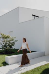 A minimalist white house exterior with concrete elements and a tree in the foreground.