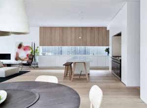 Modern residential space with white walls and wooden floors, featuring a kitchen area with wooden cabinets and white countert