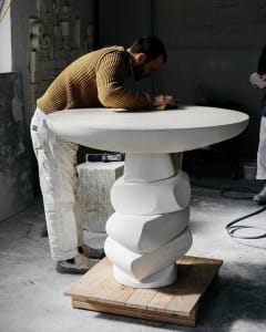 A person in a yellow sweater working with concrete in a workshop setting.