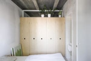 Minimalist bedroom with wooden cupboards and green potted plants on top.