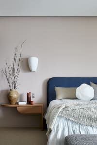 Modern bedroom featuring blue upholstered headboard, white bedding, and ceramic vase on wall-mounted shelf.