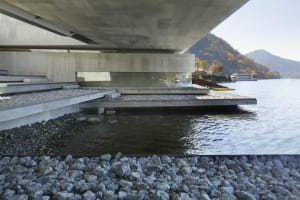 Modern waterfront residence with concrete structure and glass railings on water.