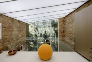 An interior space with brick walls, large glass windows, and a yellow ball on the floor.