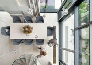 Modern dining room with grey furniture and a wooden floor, featuring a round glass table with a floral centerpiece and hangin