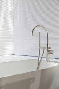 Modern bathroom with a freestanding ceramic bathtub and a sleek, minimalist stainless steel faucet against white vertical bli