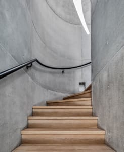 A modern concrete staircase with wooden treads and a black metal railing leading upwards.