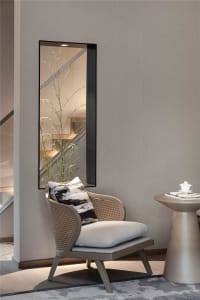 A cozy living room with a textured wall and a woven wicker chair, featuring a side table with a white teapot and a book.