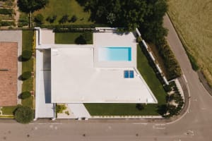 A modern house with a concrete side yard featuring a swimming pool and surrounding greenery.