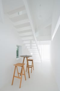 Contemporary minimalist living room with white walls, wooden furniture, and a staircase leading to another level.