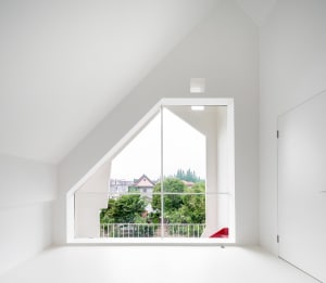 A minimalist, white-walled room with an angular window overlooking greenery.