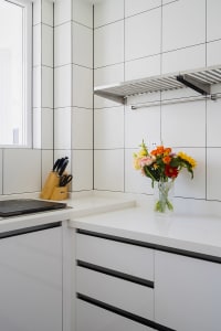 A minimalist kitchen with white ceramic tiles and black trim features a vase of colorful flowers on the countertop.
