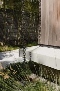 A black chain hanging down from a modern exterior wooden building with a concrete foundation and a concrete base platform.