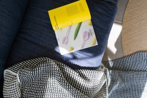 A modern living space featuring a patterned blanket draped over a footstool with a book resting on it.