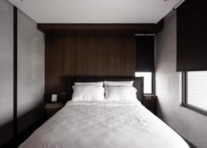 A modern minimalist bedroom with dark wood paneling and white bedding.