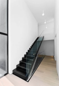 Staircase with black steps and glass railings in a minimalist interior setting.