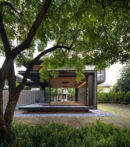 Modern house with glass walls and wooden deck surrounded by greenery.