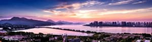 A panoramic view of a cityscape with a large body of water and a sky filled with clouds.
