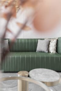A modern green leather sofa with decorative pillows in a well-lit living room setting.