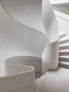 A modern, white, spiral staircase with smooth, curved walls and a soft, neutral carpet.