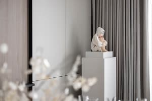 A minimalist interior with a statue of a person sitting on a pedestal.