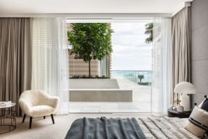 A minimalist bedroom featuring concrete walls and a large window overlooking the ocean.