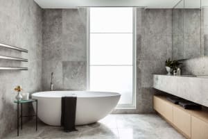 A modern minimalist bathroom with marble and concrete materials, featuring a freestanding bathtub and large window.