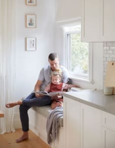 A man and a child sitting on a window sill reading a book together.