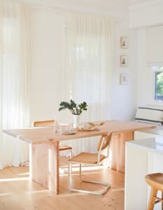 A minimalist kitchen with wooden elements, including a table and chairs, a vase with greenery, and a bread loaf.