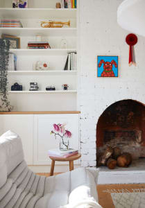 A minimalist living room with a white couch, wooden coffee table, and a white brick fireplace.