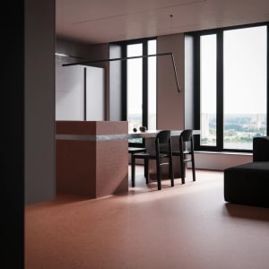 A modern kitchen with concrete and marble countertops and flooring, featuring bar stools and a view of the cityscape outside.