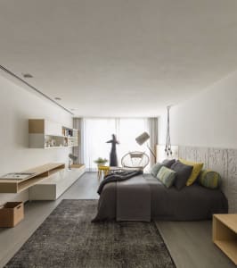 Modern minimalist bedroom with a bed, lamp, and chair near a large window.