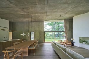 A modern living and dining space featuring a concrete ceiling and walls, with a large wooden table and chairs, a white sofa, 