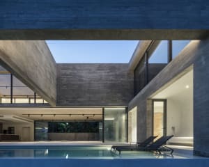 Modern residential outdoor area with a concrete pool deck and lounge chairs under structural beams.