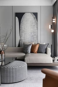 A modern living room featuring minimalist artwork, a comfortable sofa, and a round ottoman with a black and white pattern.