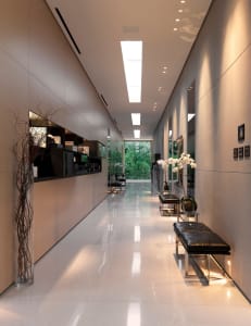 Modern interior design featuring glass and concrete materials in a long corridor with a view of greenery.