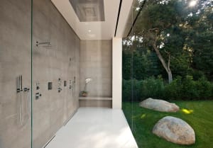 Modern minimalist bathroom interior with concrete walls, glass enclosure, and garden view.