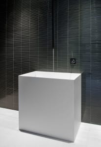 A minimalist white porcelain basin against a dark, striped wall background, highlighting sleek and contemporary design.