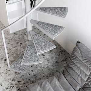 A modern grey staircase features a white metal railing on a terrazzo floor.